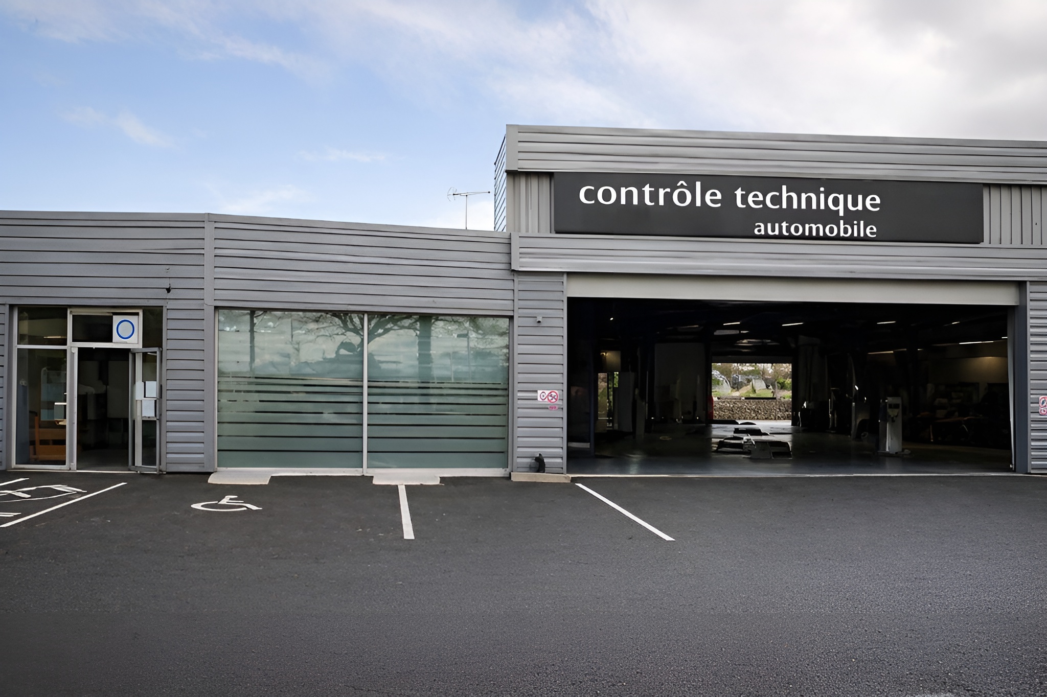 Façade d’un centre de contrôle technique automobile avec baie ouverte, parking devant le bâtiment et utilitaire blanc à l’intérieur.