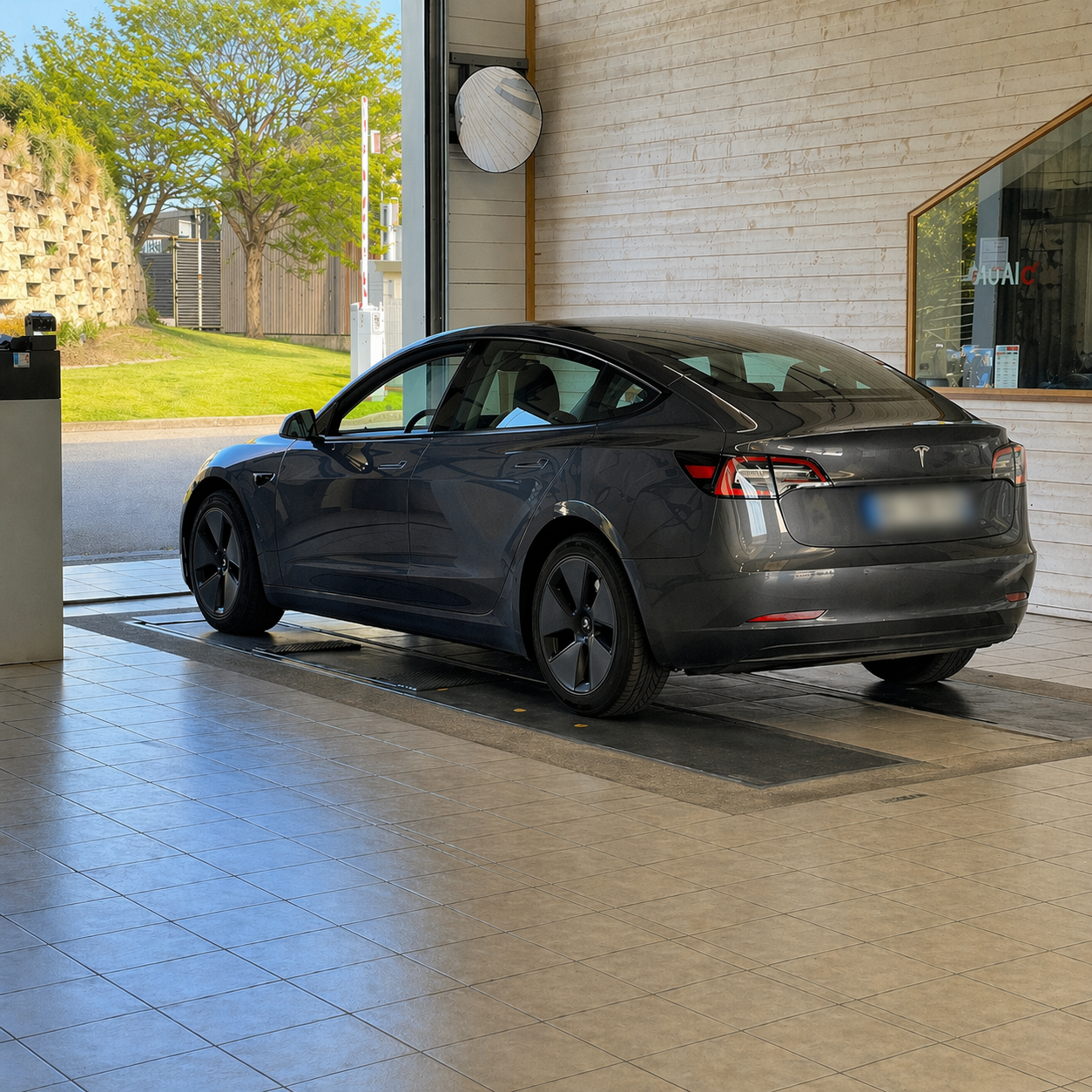 Tesla grise stationnée sur une ligne de contrôle technique dans un atelier moderne et lumineux, avec vue dégagée sur l’extérieur.